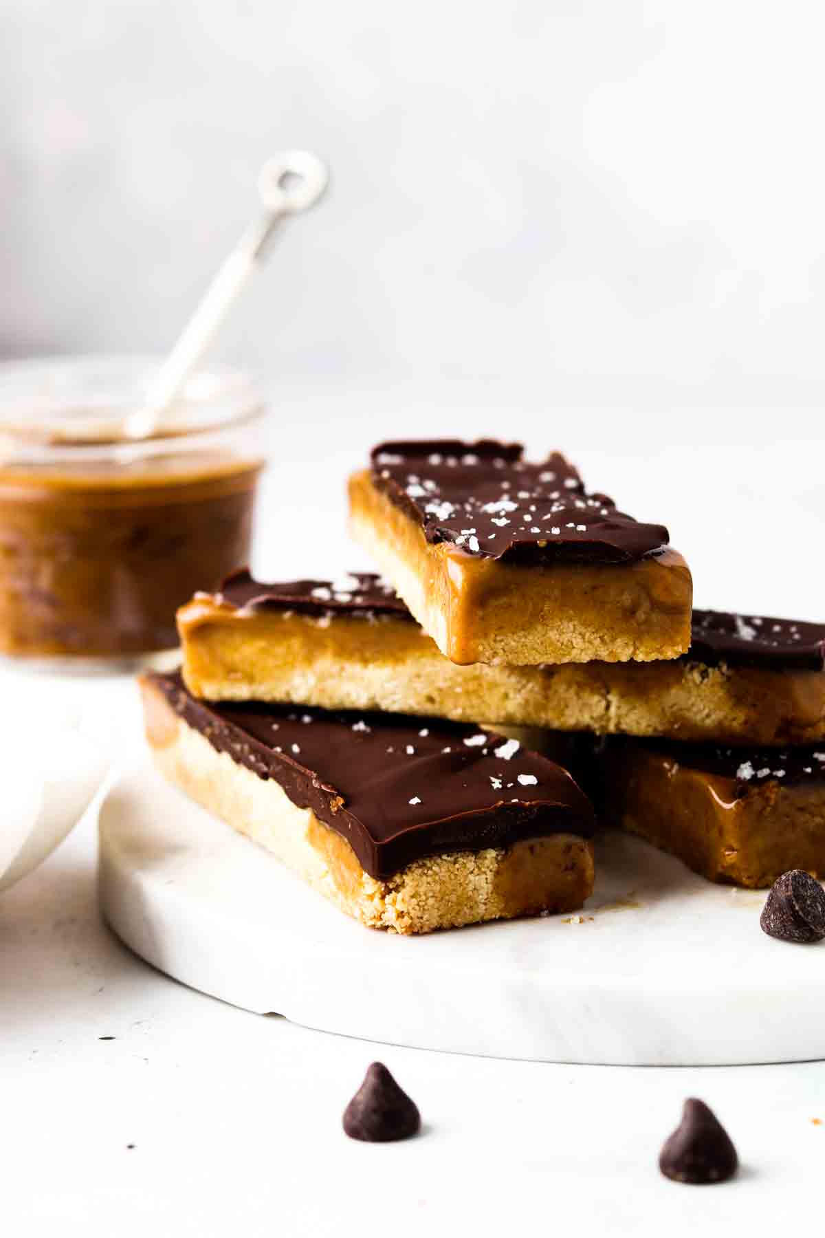 4 twix bars on a marble plate with a bowl of caramel sauce on the side. 