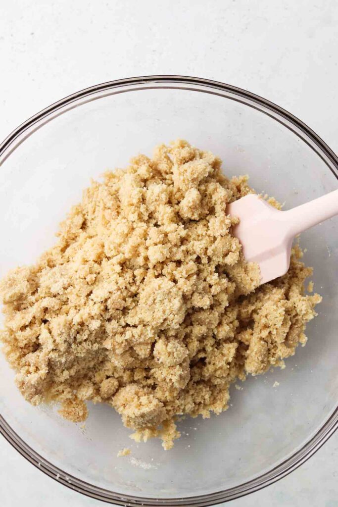 Well mixed shortbread crust in a clear bowl with a pink spatula. 