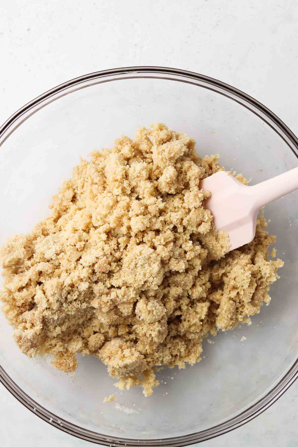 Well mixed shortbread crust in a clear bowl with a pink spatula.