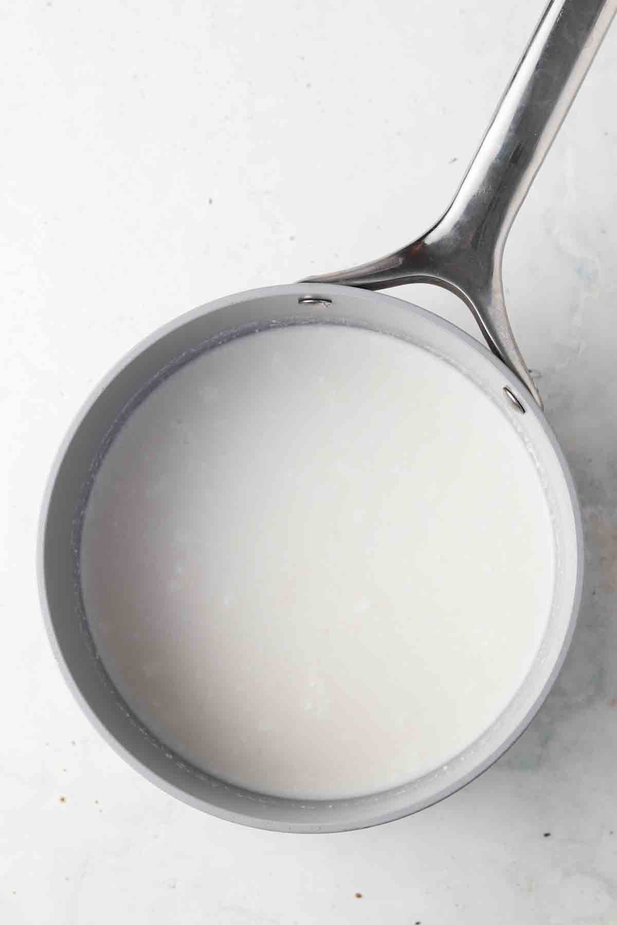 Coconut milk in a sauce pan on the stove top.