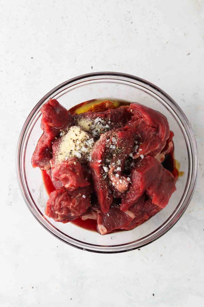 raw steak marinating in a bowl