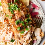 blackened cod on a plate with slaw and lemons