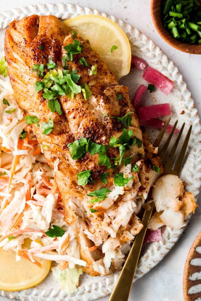 blackened cod on a plate with slaw and lemons