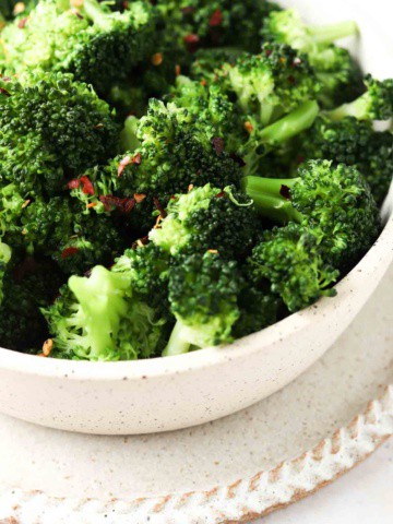 Broccoli in a bowl with red pepper flakes and salt on top.