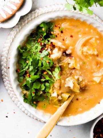 cauliflower and leek soup in a bowl with fresh herbs on top