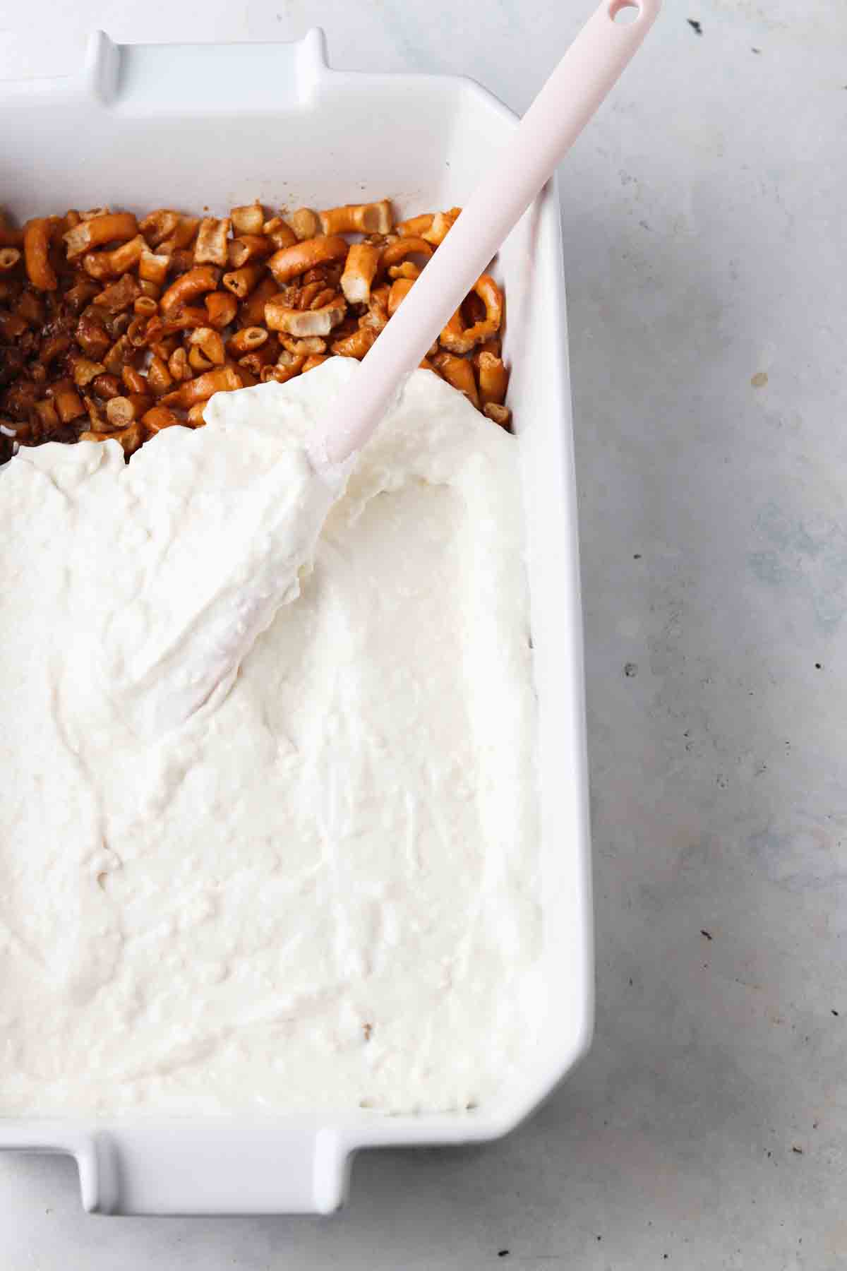 Cream cheese and whipped cream being spread over pretzel layer.