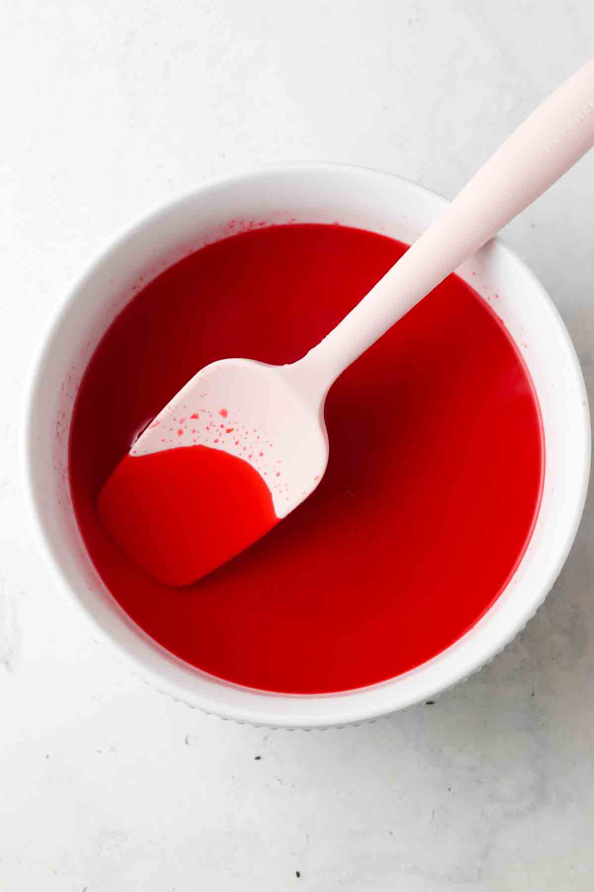 Jello mix in water in a white bowl with a pick spatula. 