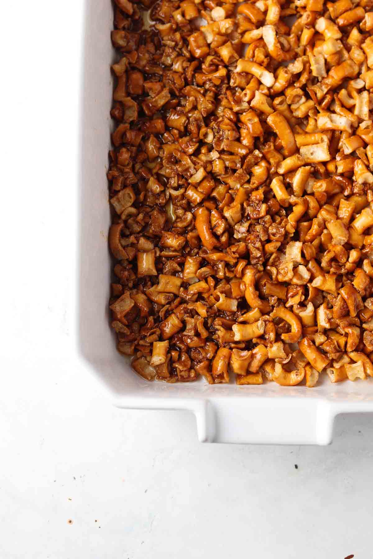 Pretzel, ghee, and coconut sugar mixture spread in the bottom of a white casserole dish.