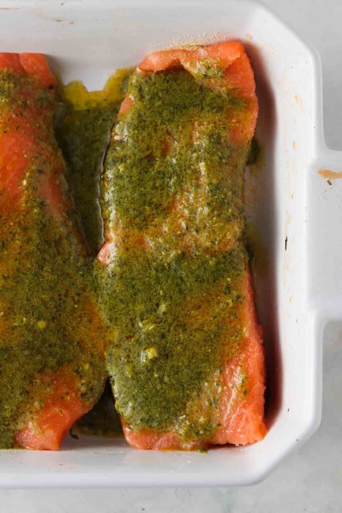 salmon in a baking dish with pesto sauce on top