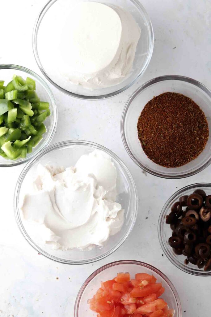 cream cheese, sour cream, taco seasoning, olives, tomatoes, and peppers in bowls