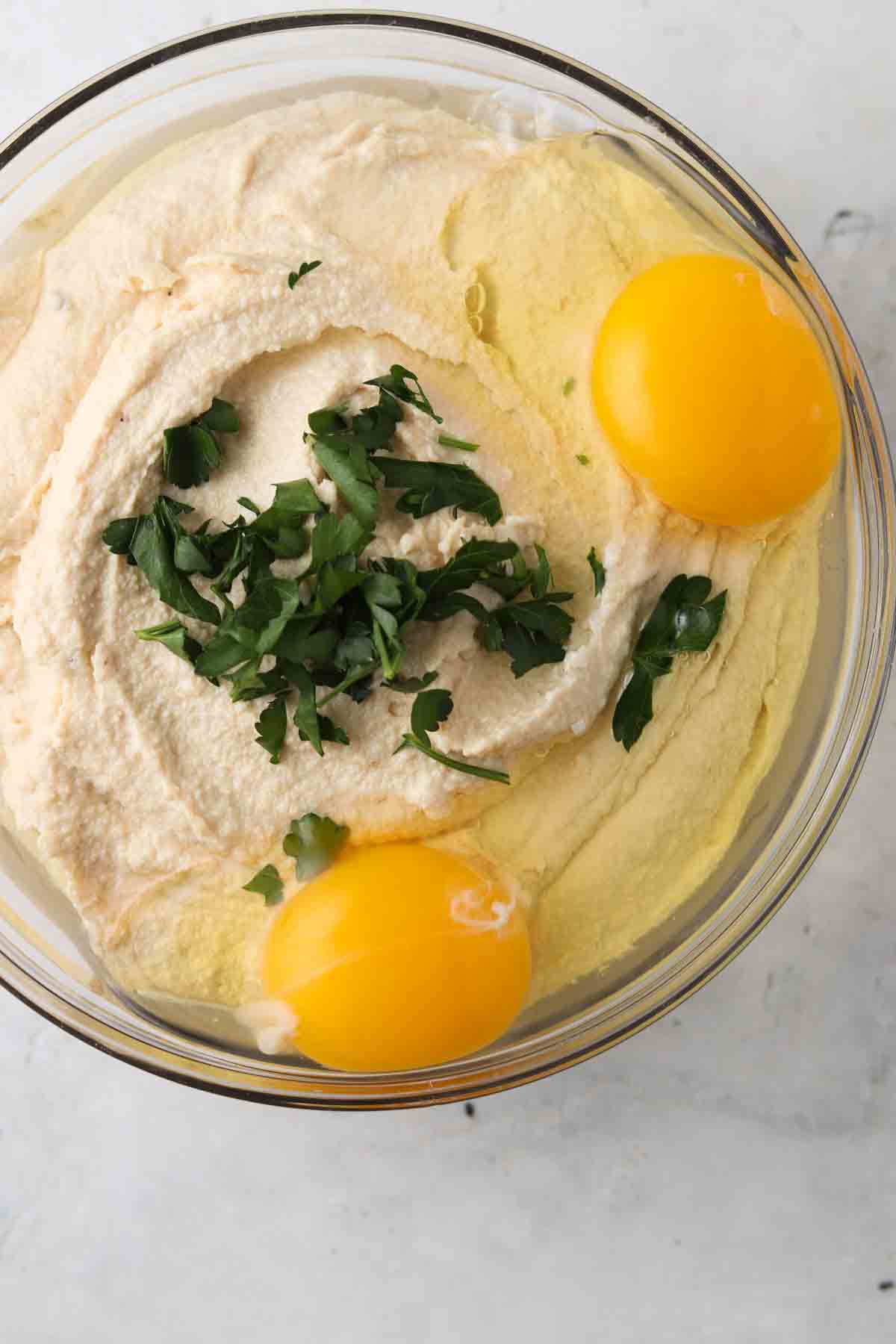 Cashew cheese, eggs and parsley in a glass bowl.