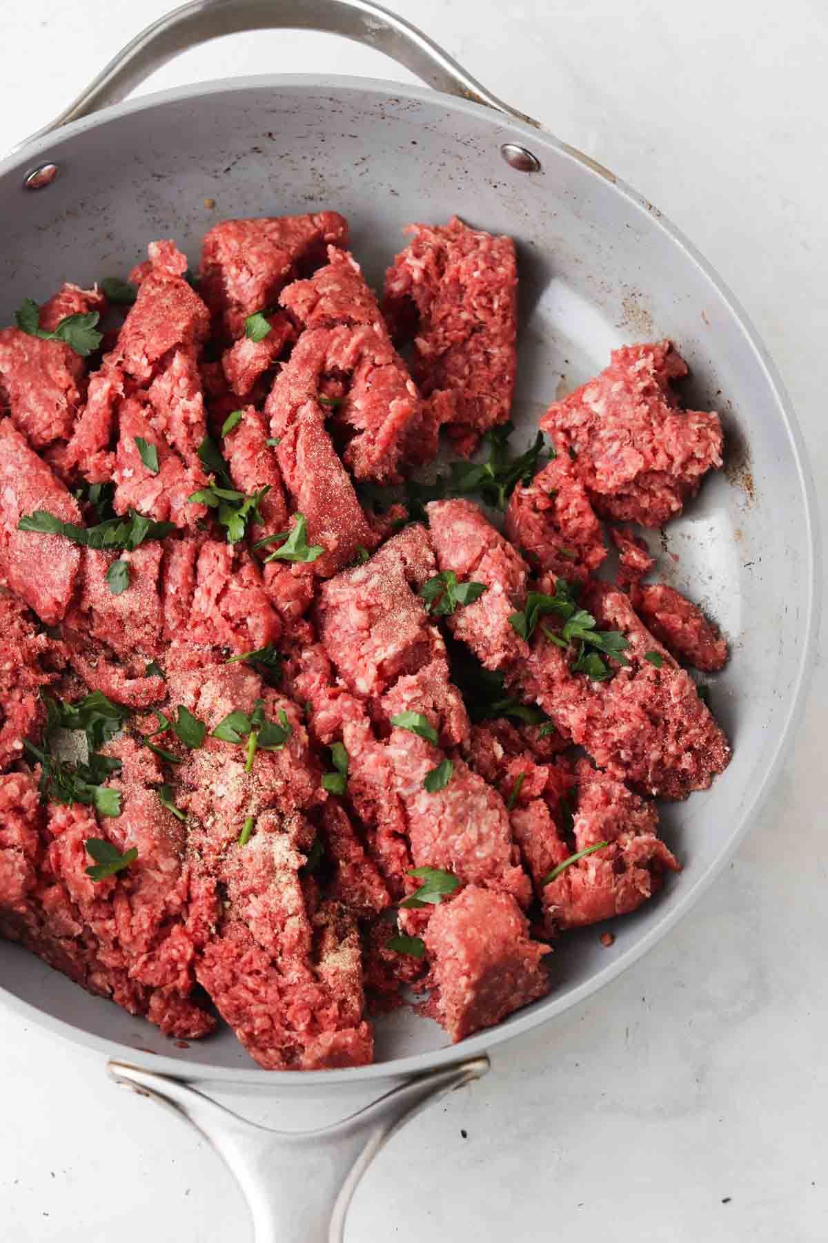 Ground beef and herbs in a grey saute pan.