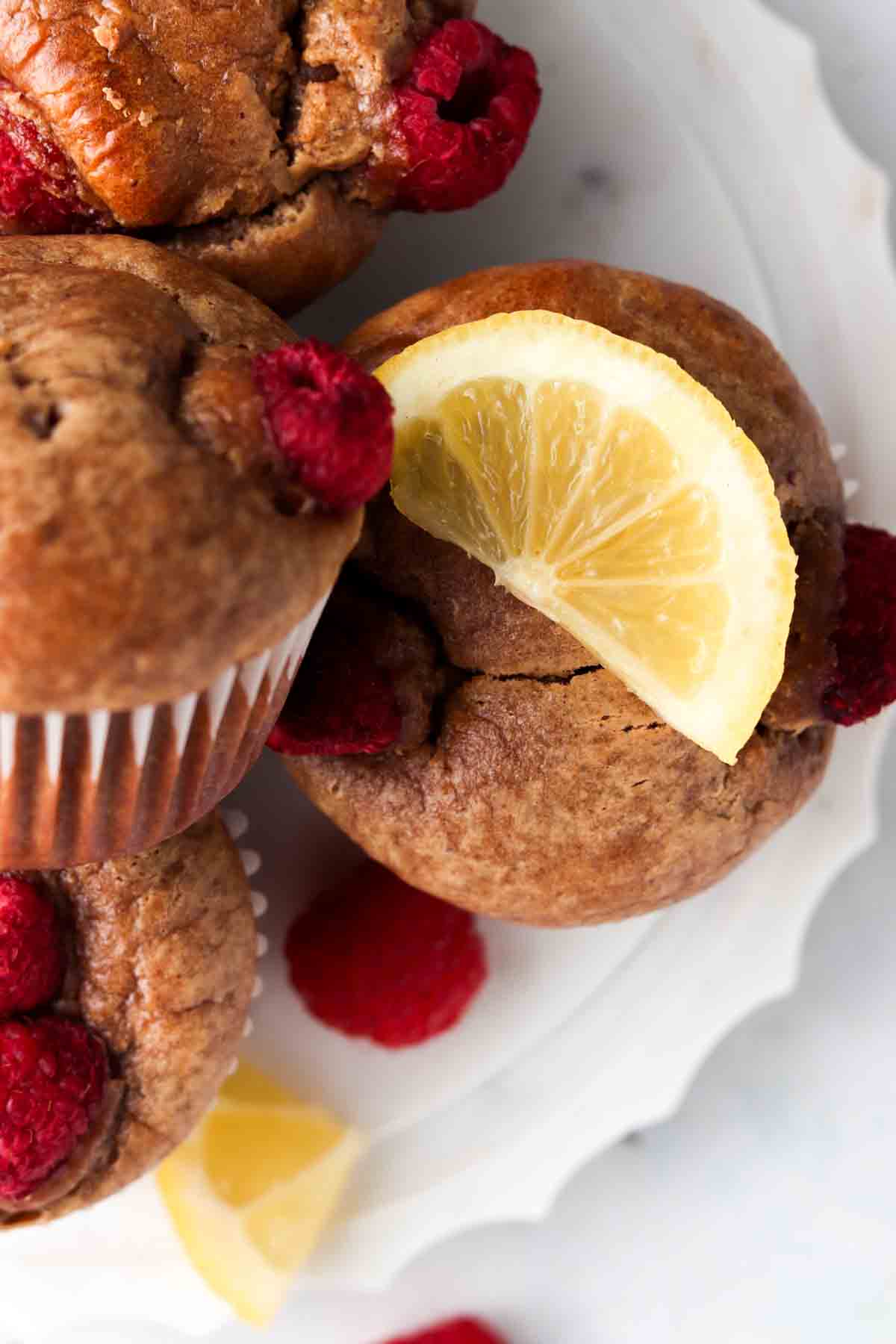 Raspberry muffins with a lemon wedge on top on a white plate.