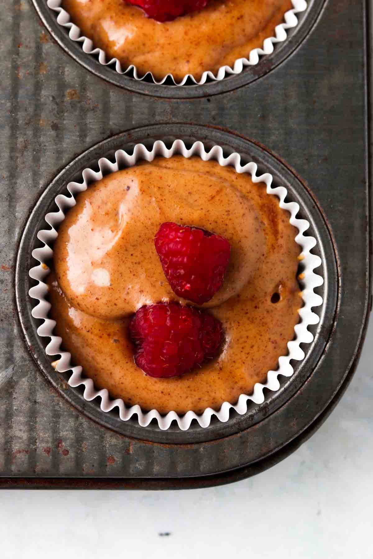 Raspberries on top of muffins in muffin pan.