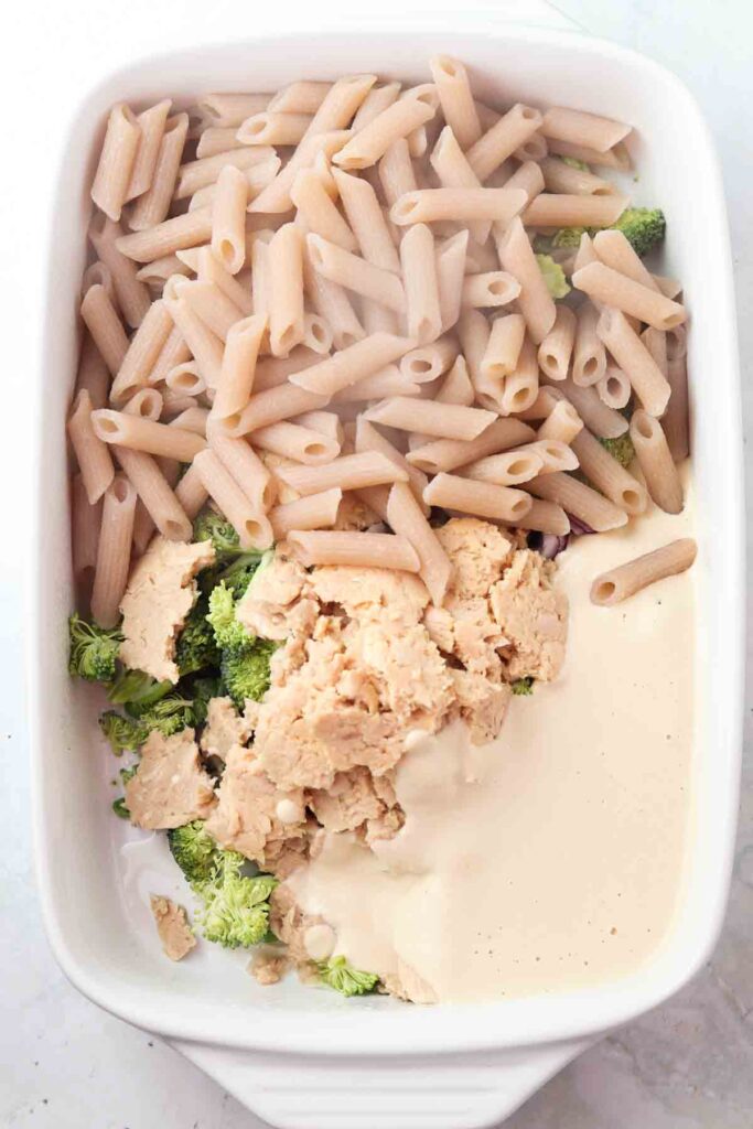 tuna noodle casserole ingredients in a casserole dish- cashew cheese, pasta, broccoli, peas, and tuna in a casserole dish