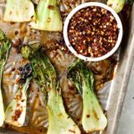 roasted bok choy on a sheet pan with red pepper flakes on top