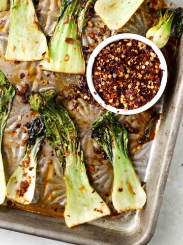 roasted bok choy on a sheet pan with red pepper flakes on top