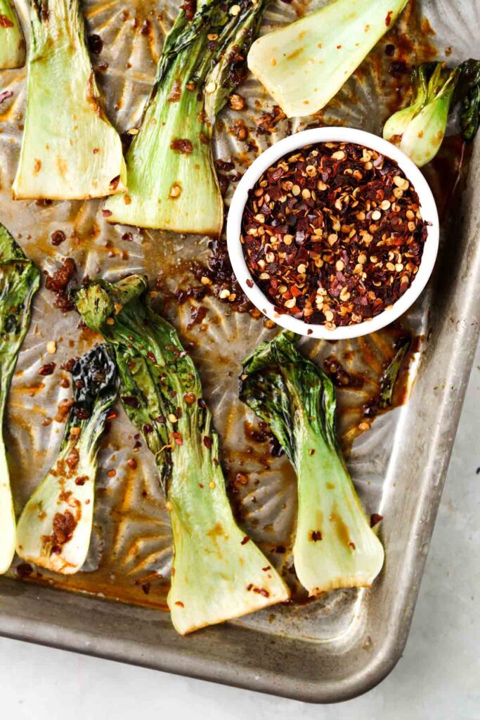 roasted bok choy on a sheet pan with red pepper flakes on top