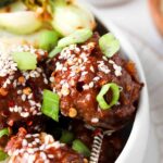 asian meatballs in a bowl with sesame seeds and green onions on top