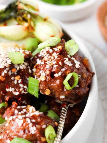 asian meatballs in a bowl with sesame seeds and green onions on top