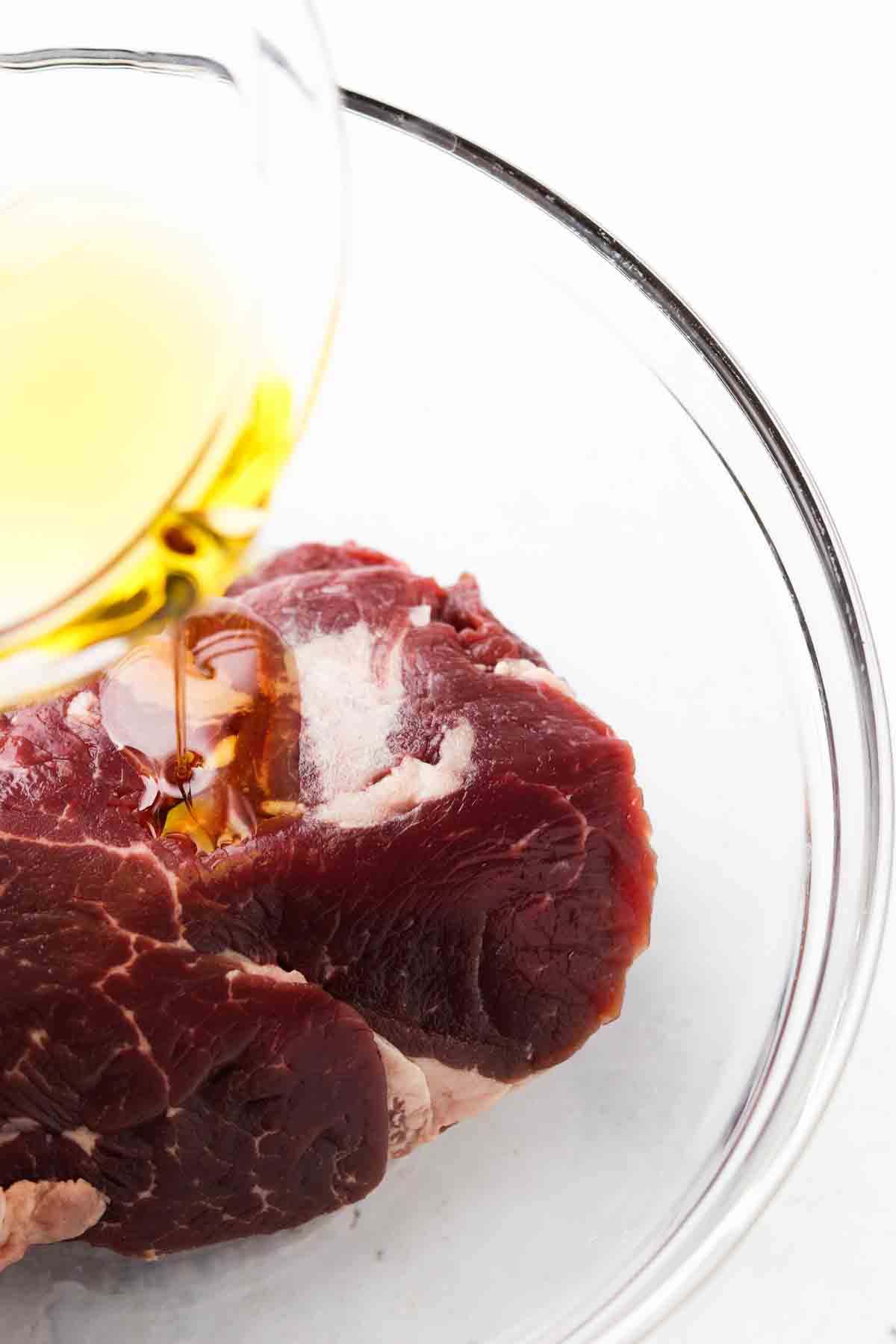 Butter on top of steak in a glass bowl.