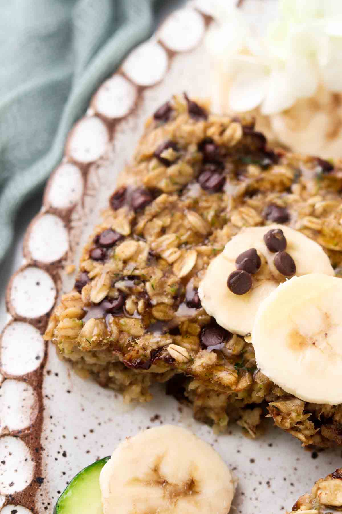 Zucchini chocolate chip oatmeal bars on a plate with fresh banana and chocolate chips. 