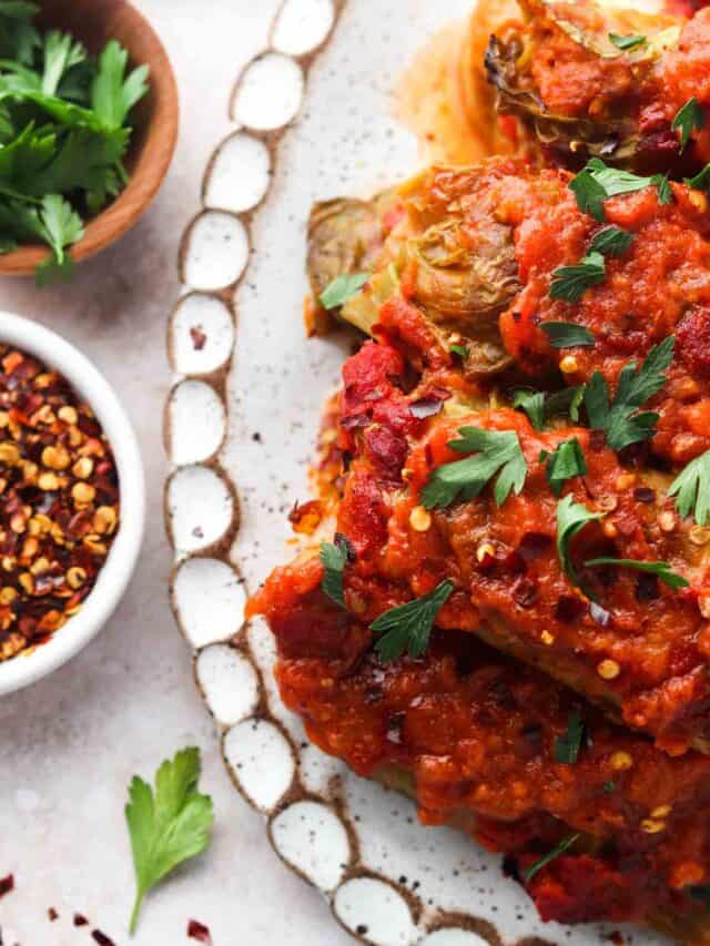 Stuffed cabbage rolls topped off with fresh parsley on a white plate with red pepper flakes.