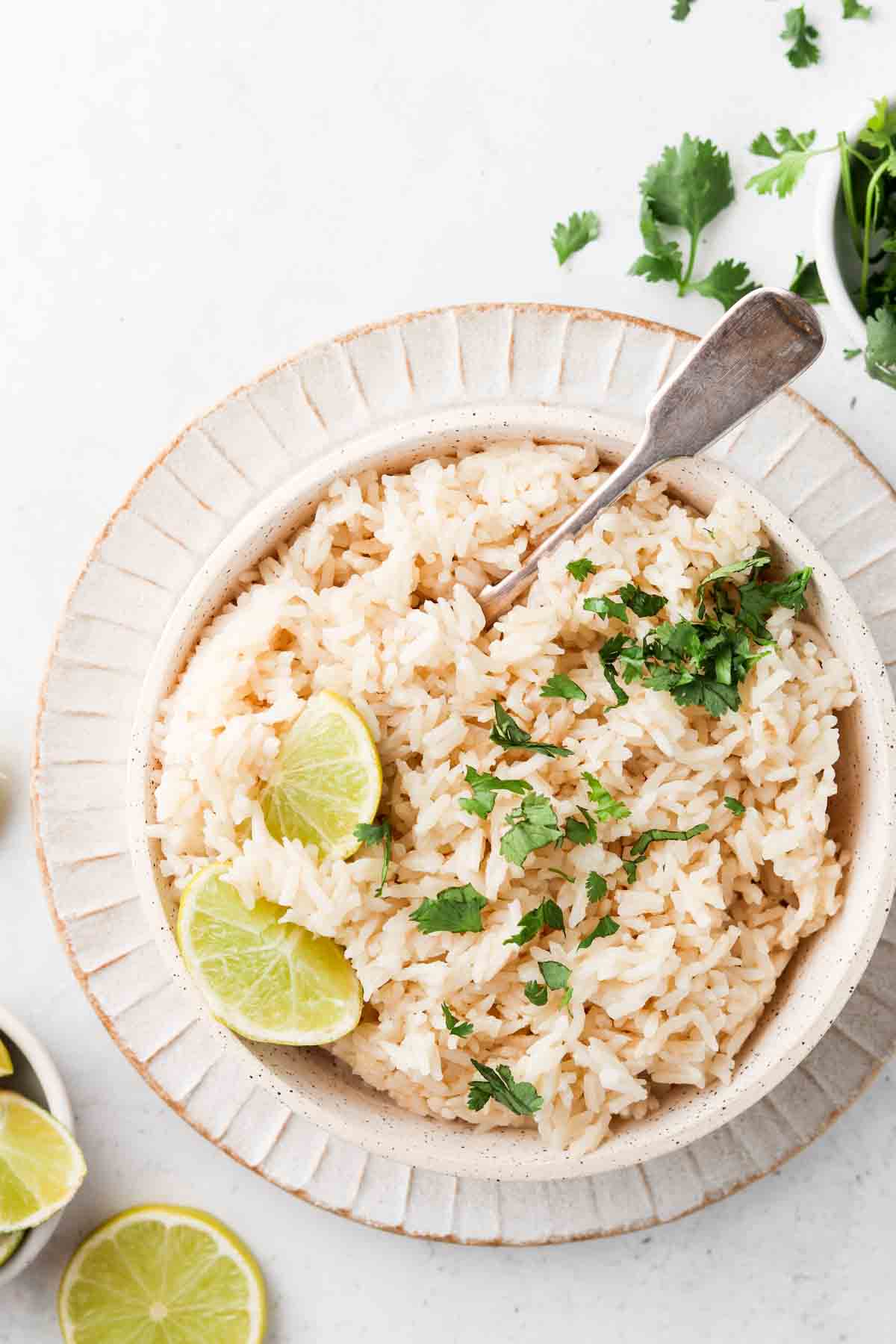 Overhead shot of coconut rice in a bowl with fresh limes and herbs on top.