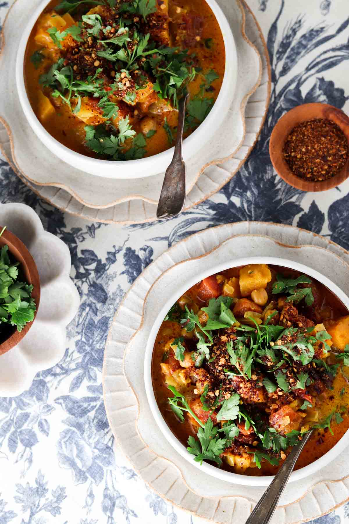 Overhead photo looking down at two bowls of chickpea curry with fresh herbs and red pepper flakes on top.