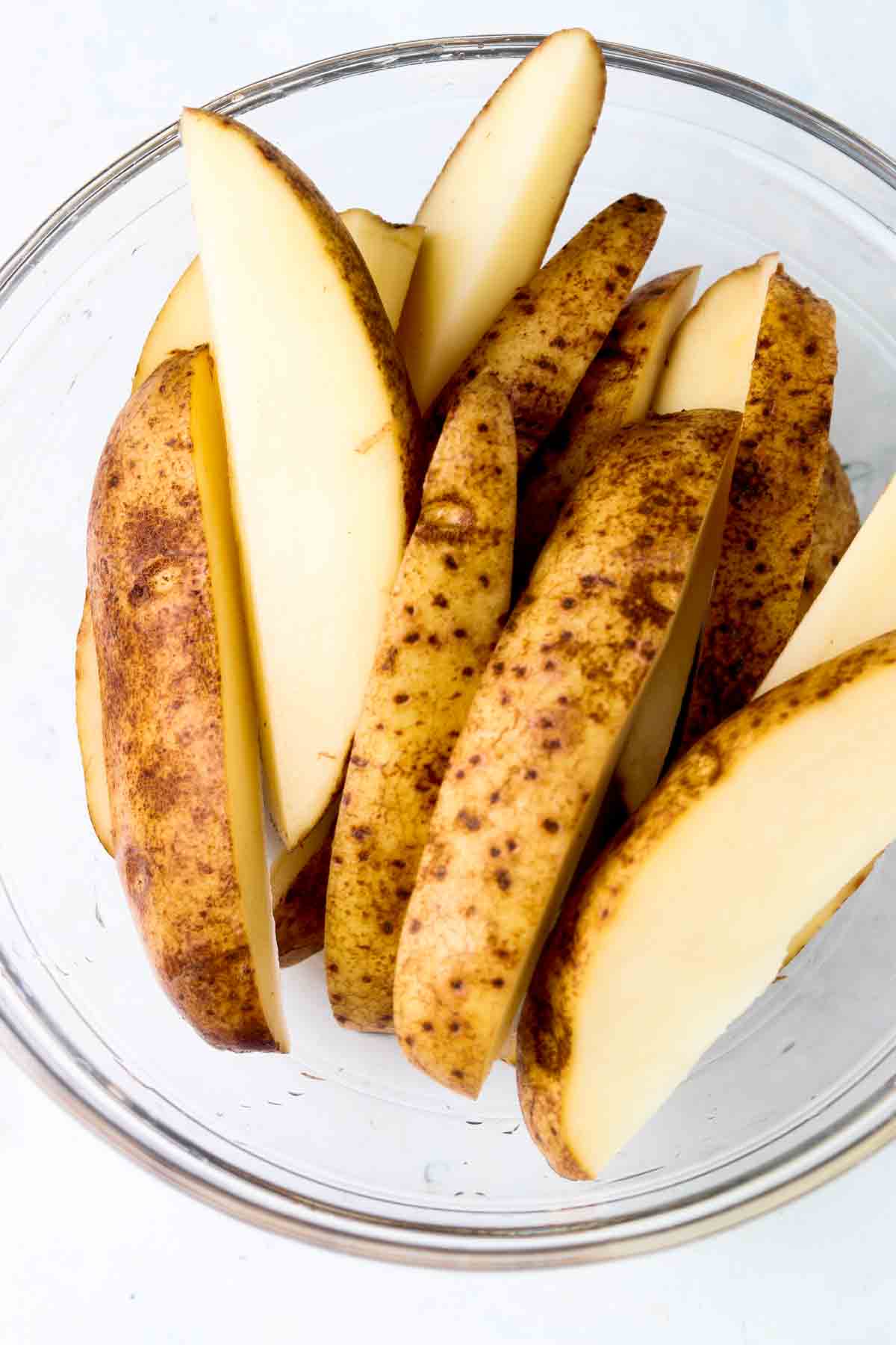 Cut up potato wedges in a glass bowl.
