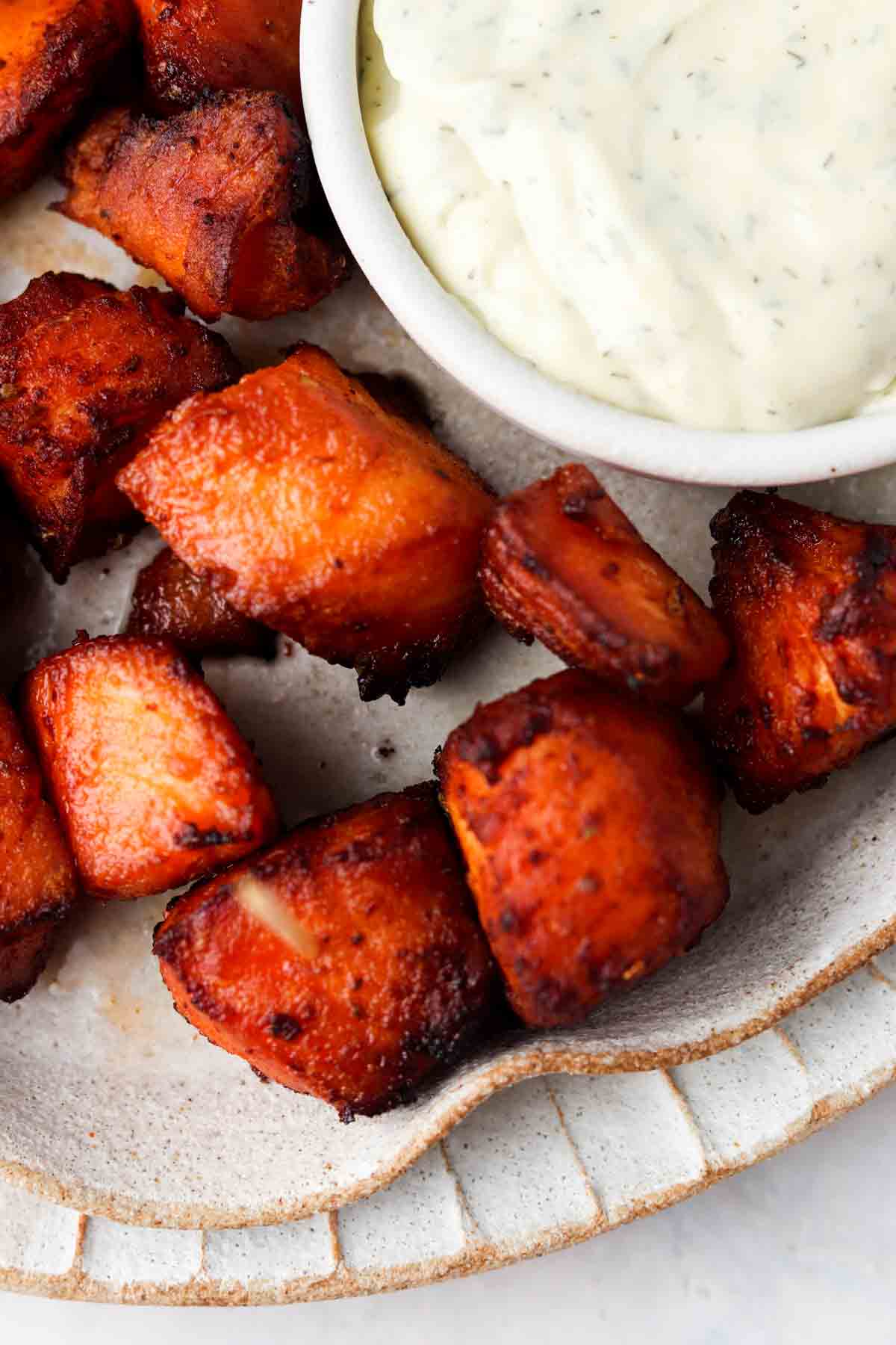 Salmon bites on a plate next to a white bowl of dressing.