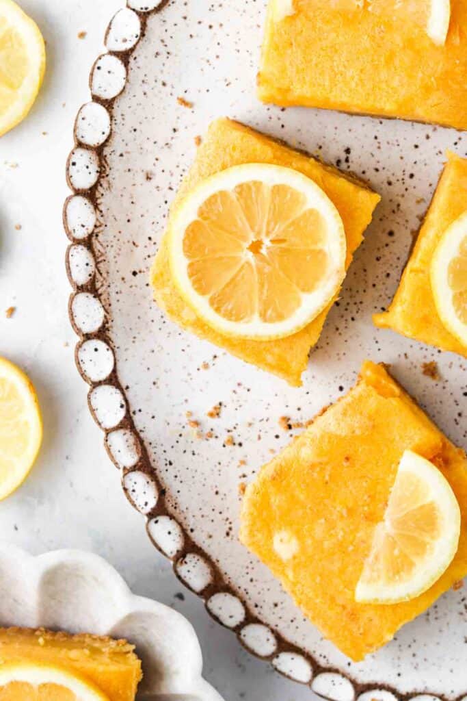 Gluten Free Lemon Bars on a plate with speckles all over it.