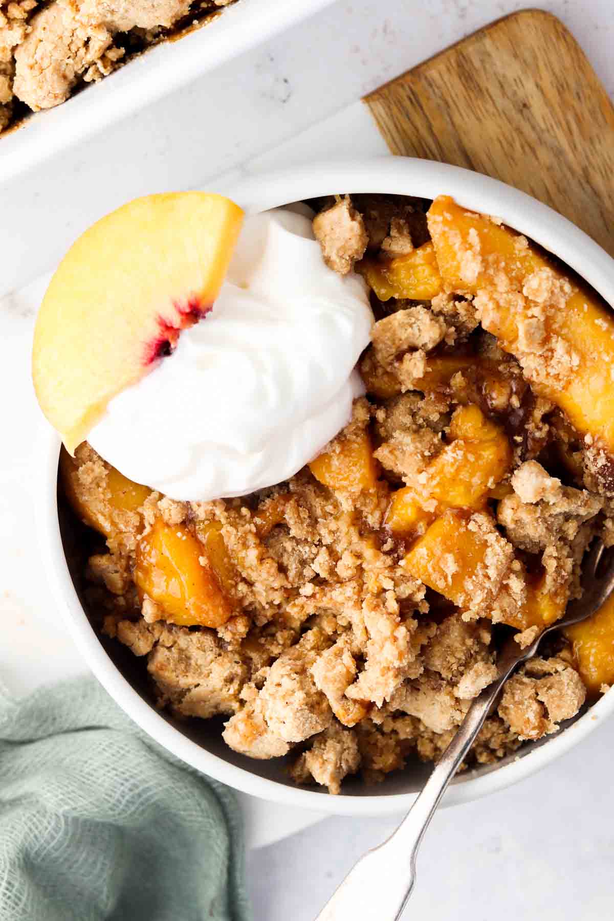 Peach cobbler in a serving dish with a spoonful of dairy free whipped cream and a peach slice.