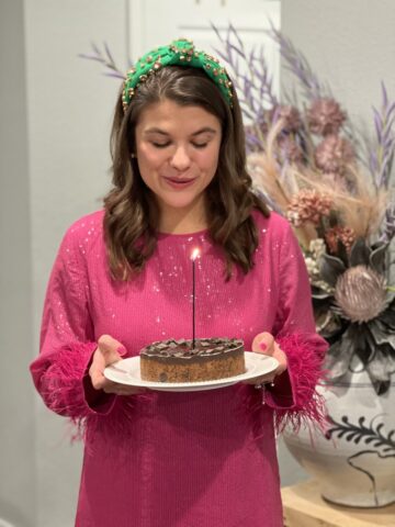 Allianna Moximchalk in a pink dress with a green headband on holding a cookie cake with a candle in it.