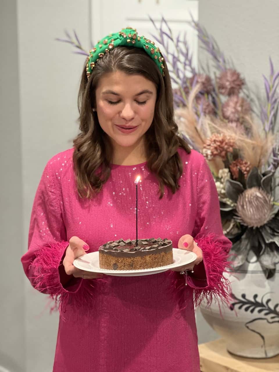 Picture of Allianna Moximchalk in a pink dress with a green headband holding a cookie cake with a candle in it.