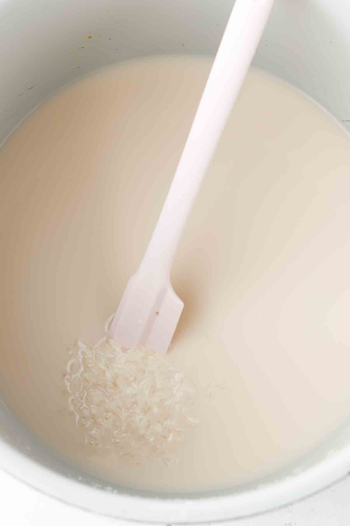 White rice, coconut milk, sea salt and bone broth in an instant pot with a silicone spoon,