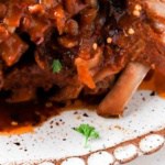 Baby back ribs on a plate with red pepper flakes and fresh parsley sprinkled on top.