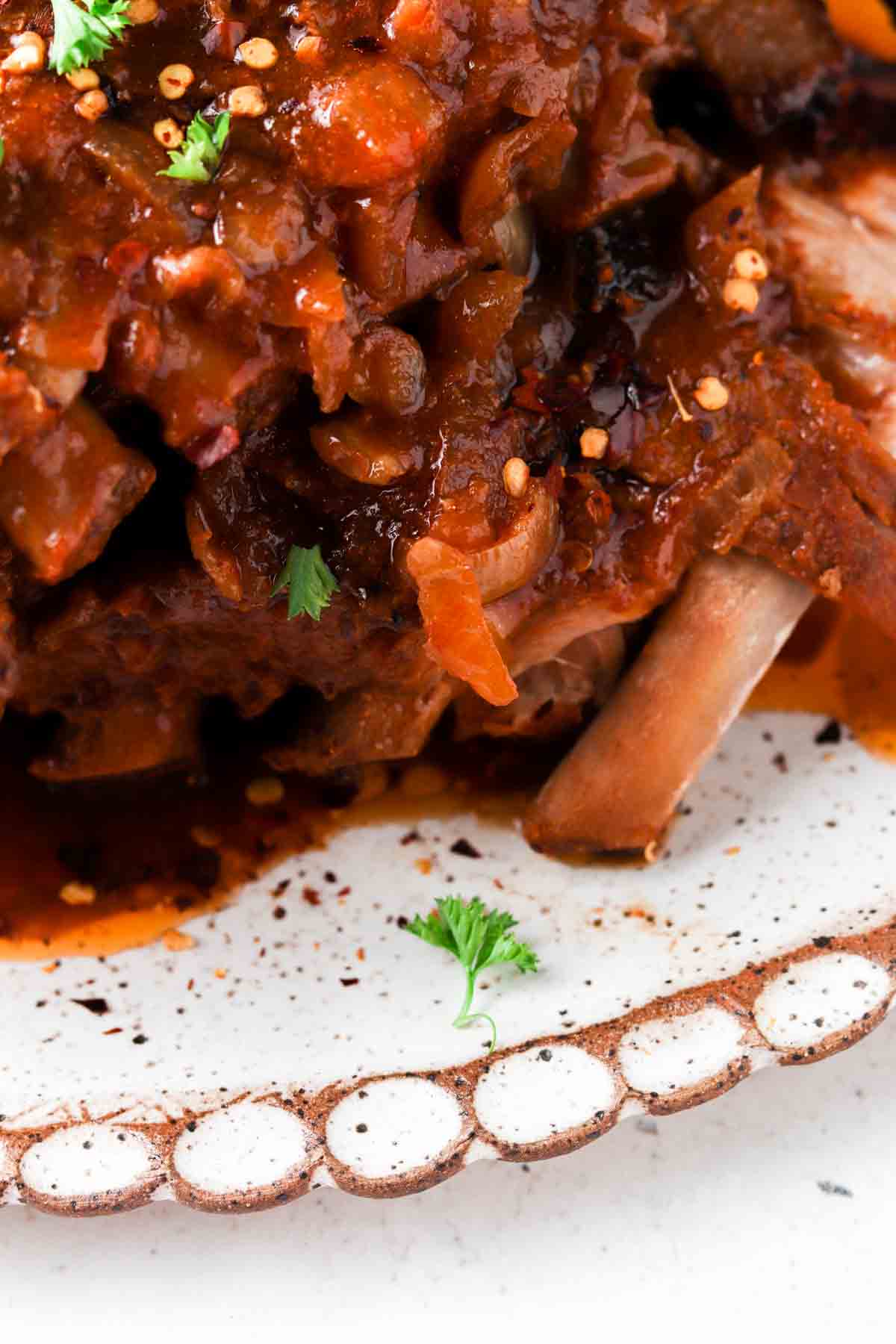 Baby back ribs on a plate with red pepper flakes and fresh parsley sprinkled on top.