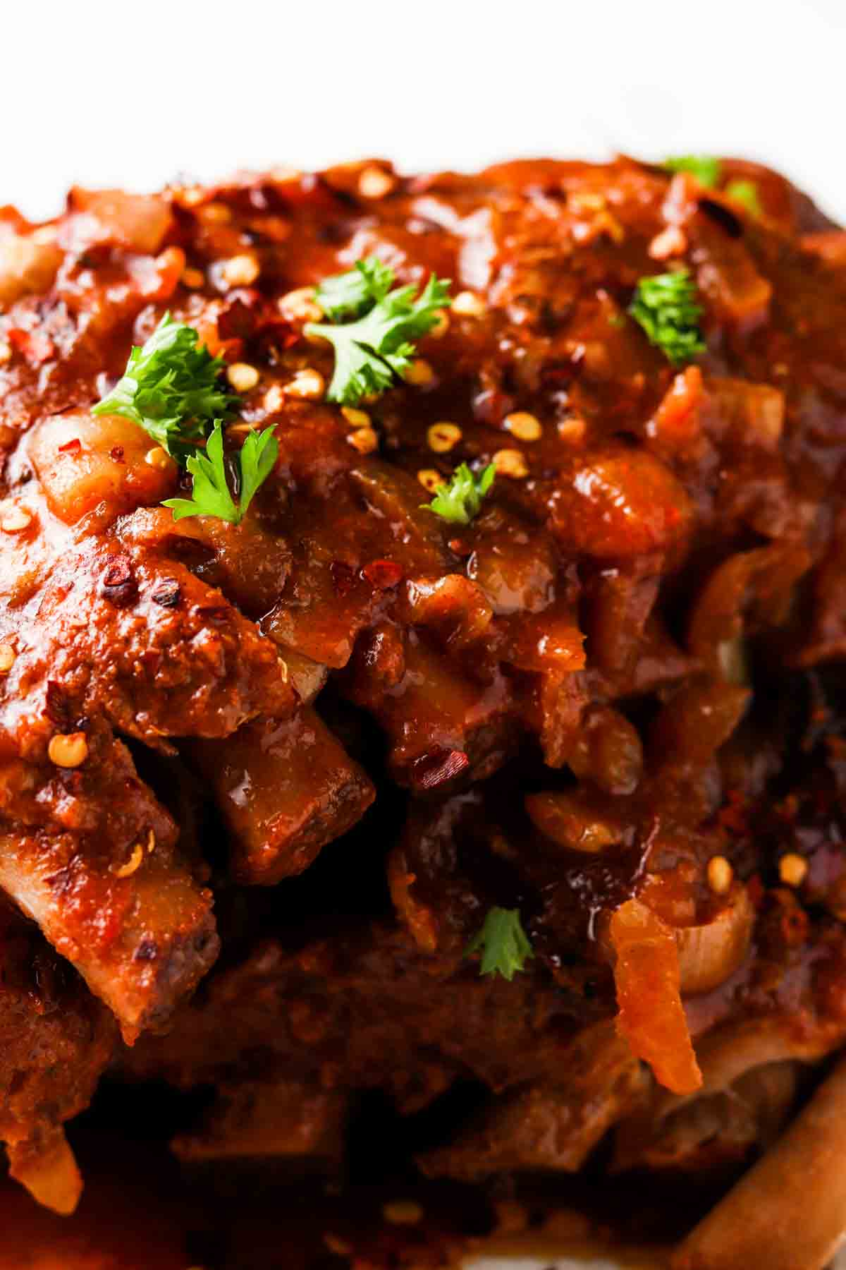 Overhead shot of baby back ribs on a platter with fresh herbs and red pepper flakes. 