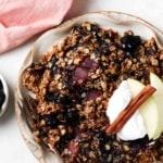 Apple and blueberry crumble on a plate with whipped cream and apple slices on top.