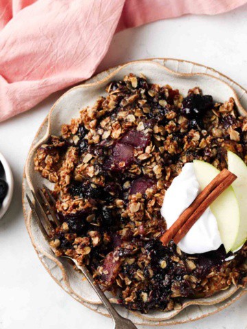 Apple and blueberry crumble on a plate with whipped cream and apple slices on top.