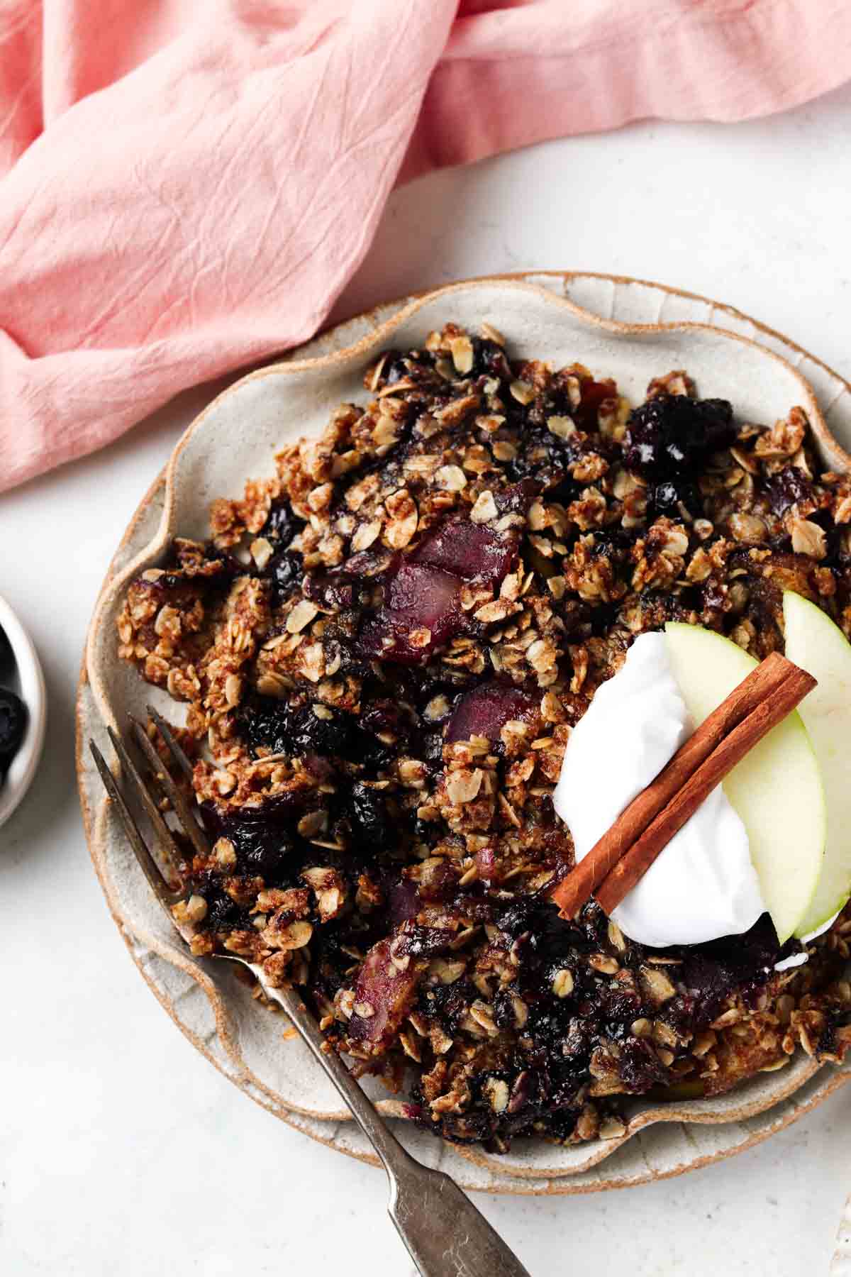 Apple and blueberry crumble on a plate with whipped cream and apple slices on top.