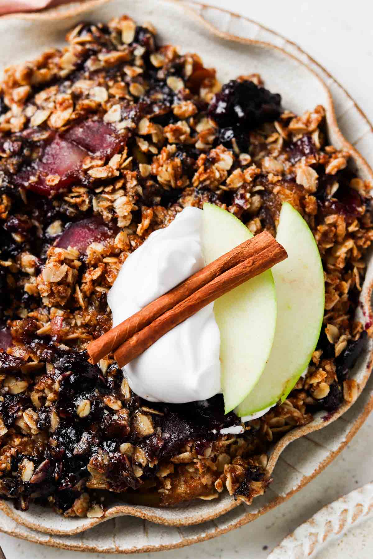 Close up photo of a blueberry and apple dessert on a plate with whipped cream and apple slices. 