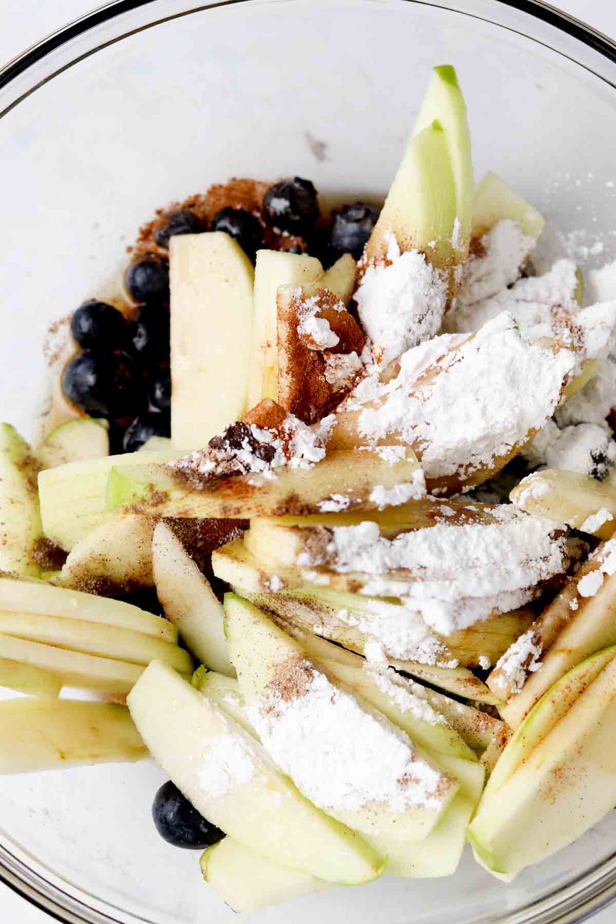 Blueberries, apples, arrowroot, cinnamon, cardamom, vanilla, and maple syrup in a bowl.