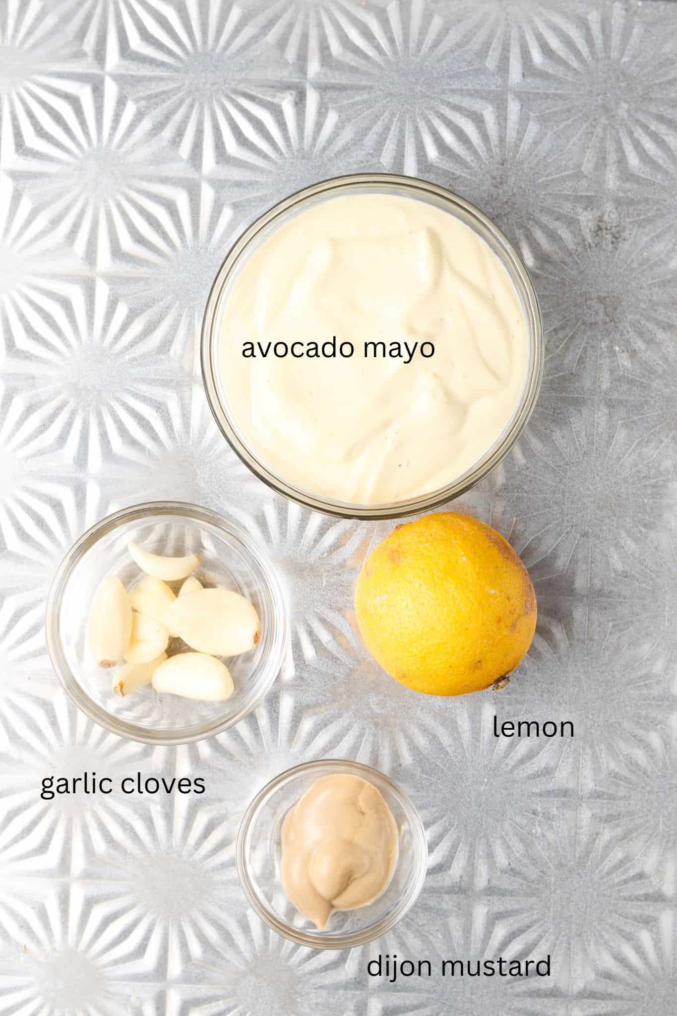 Garlic aioli ingredients laid out in small glass bowls on a sheet pan. 
