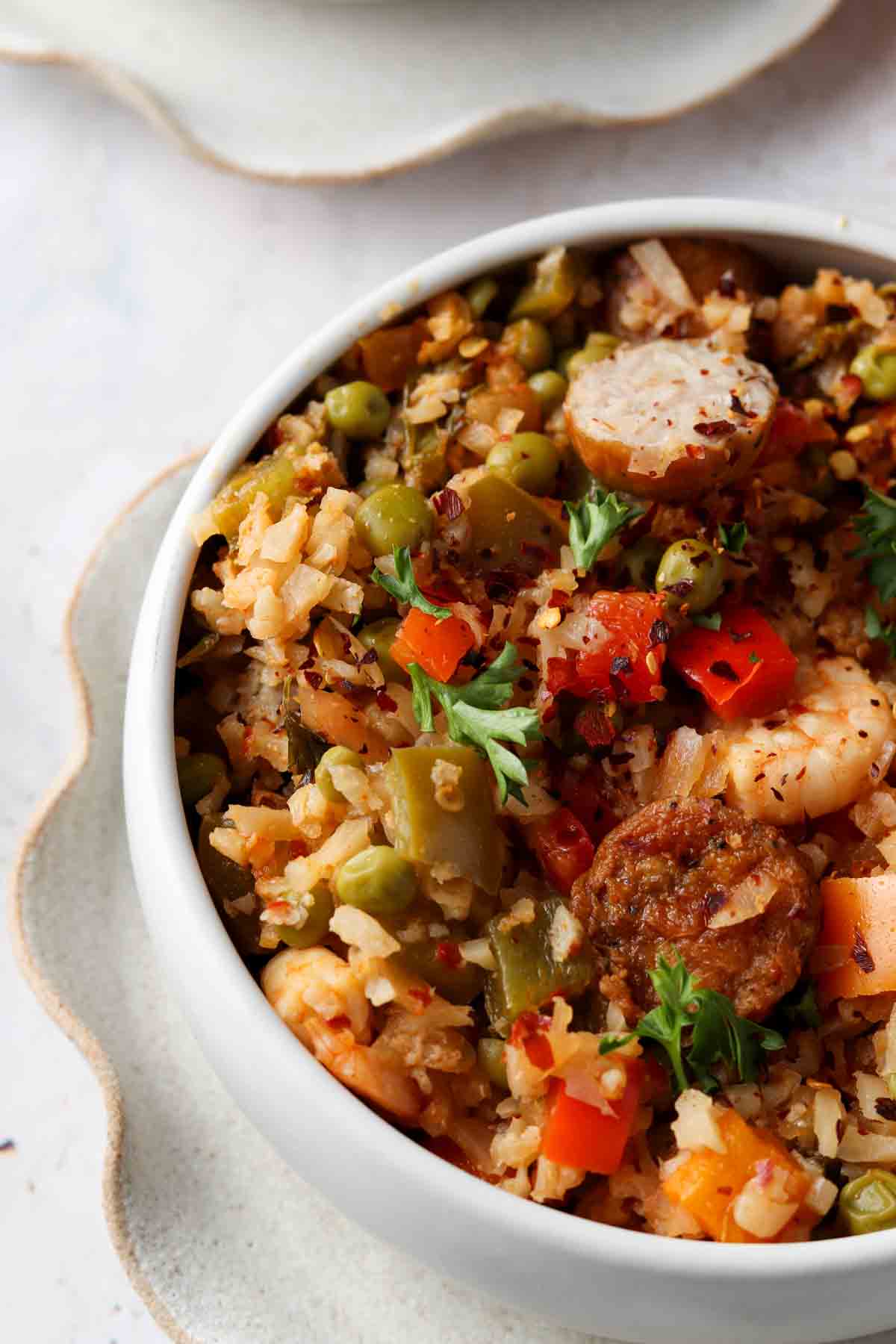 Paella with shrimp and sausage on top in a pretty bowl with a ruffled plate underneath. 