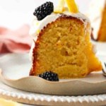 Close up photo of a piece of cake on a plate with blackberries and lemons on top.