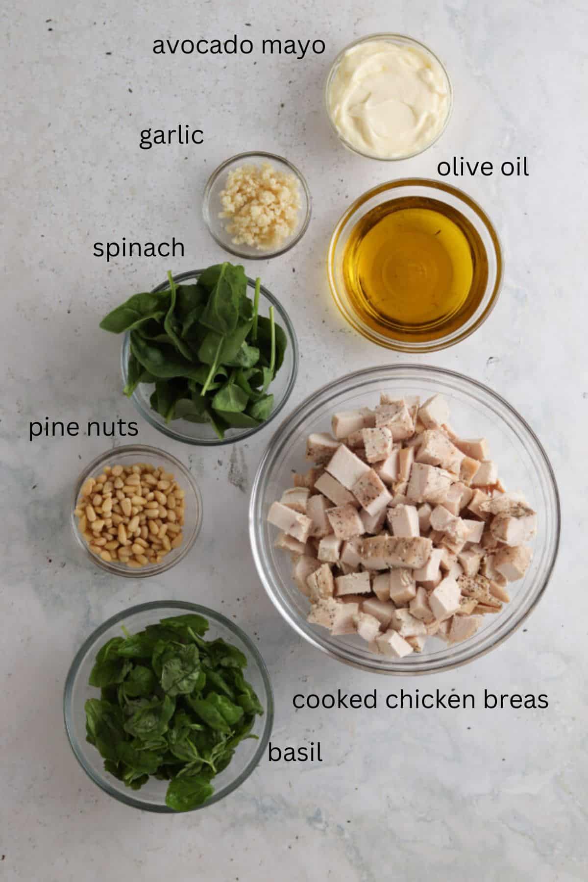 Labeled pesto chicken salad ingredients in small glass bowls. 