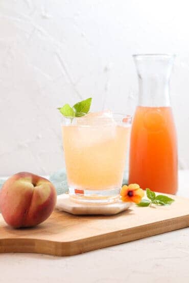 Peach basil mocktail garnished with fresh basil with a whole peach next to it.