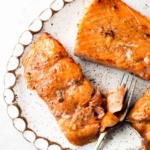 Cooked salon filets with pepper on top on a scalloped white tray with a fork on the side.